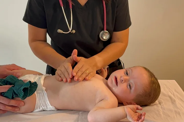 Las manos de Constanza sobre el pecho de un bebé tumbado boca arriba, durante una sesión de fisioterapia respiratoria.