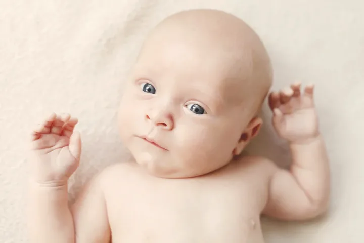 Bebé tumbado boca arriba sobre una manta clara, con la cabeza inclinada hacia un lado.